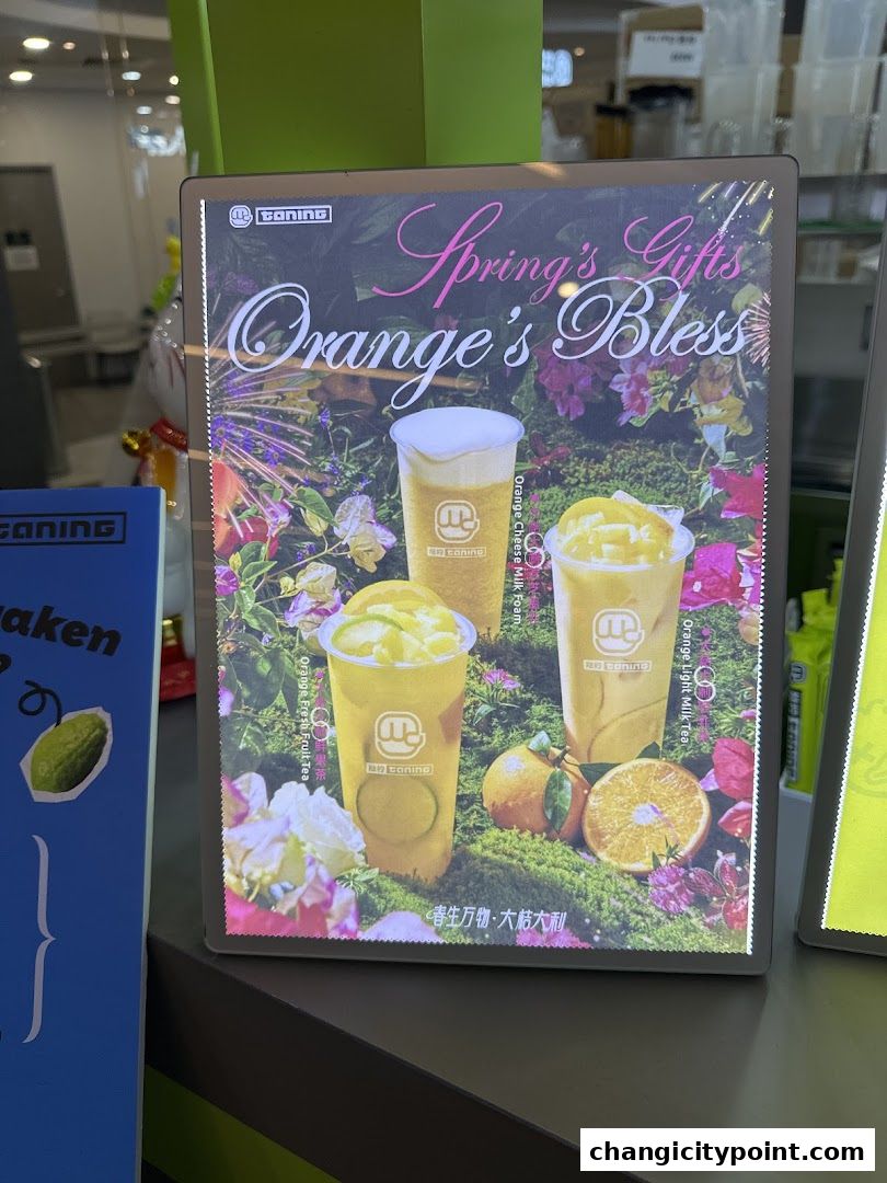 A promotional sign for Taning's 'Orange's Bless' drinks with floral and orange imagery.