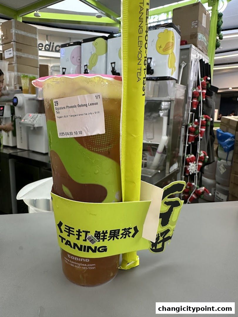 A close-up of a large cup of oolong lemon tea with a yellow straw and cup holder.