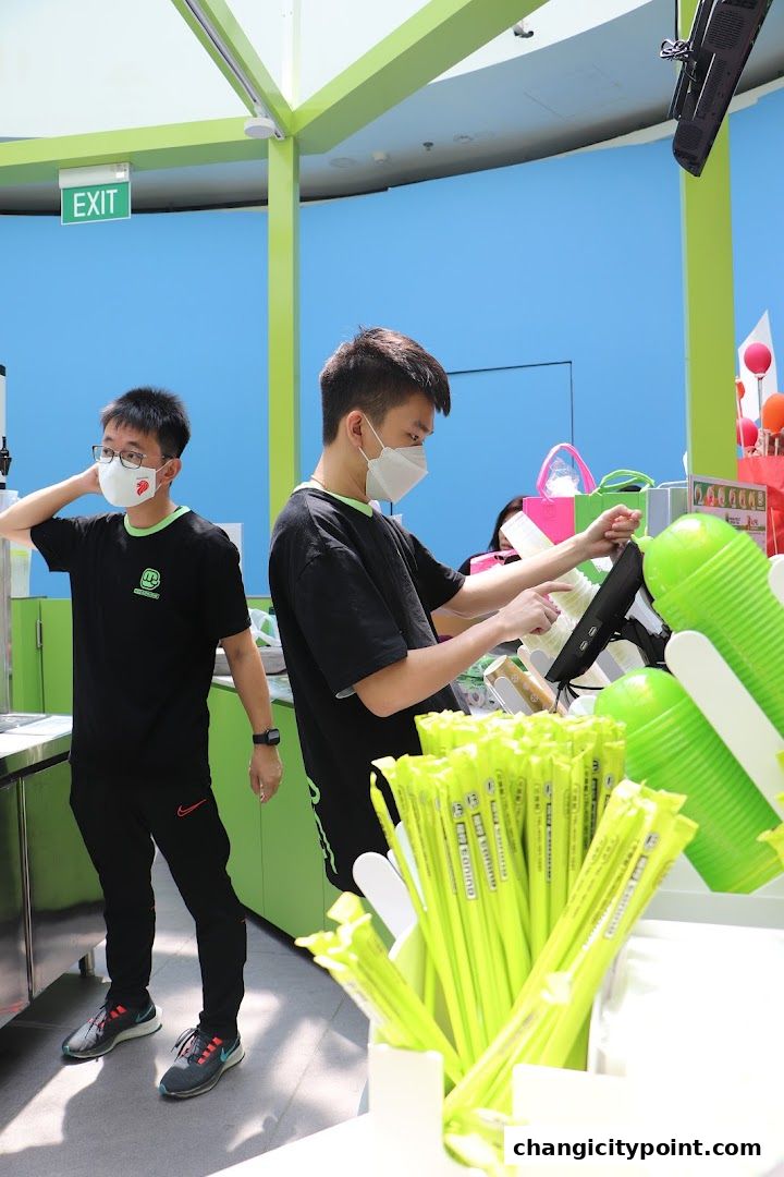 Two staff members wearing masks work behind a counter with green straws and cups.