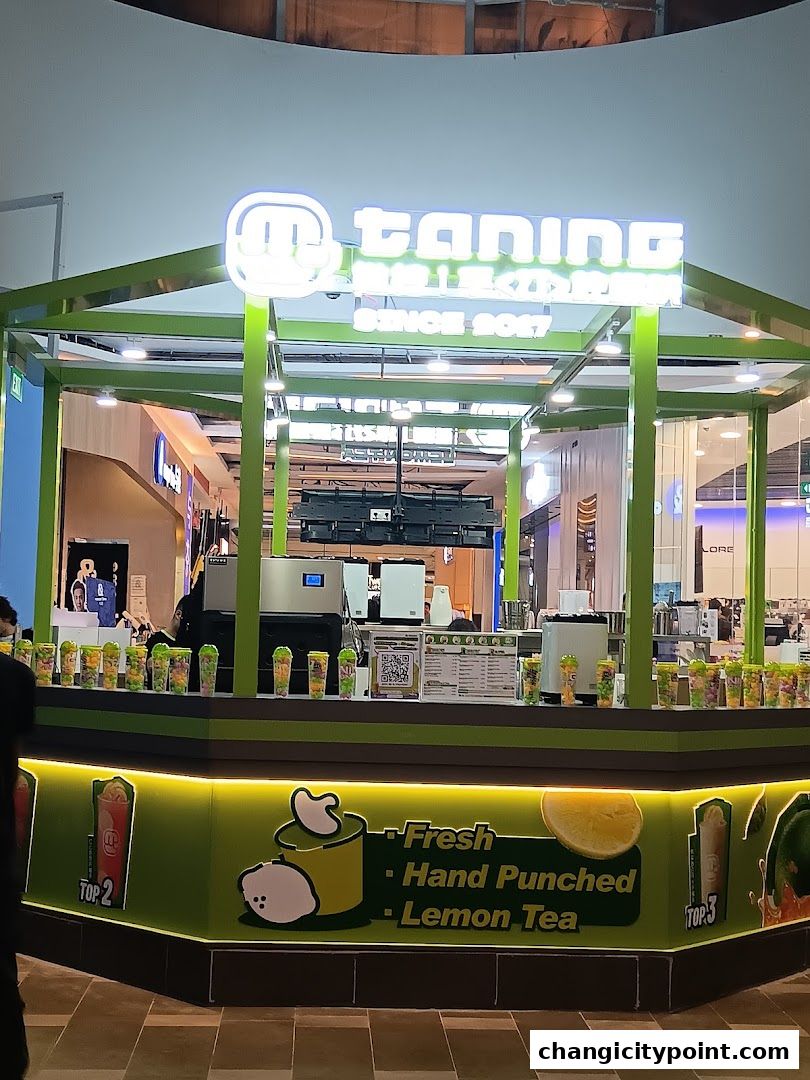 A brightly lit beverage stall with a neon sign and colorful drinks displayed.