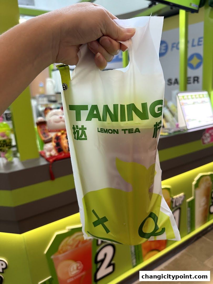 A hand holds a Taning Lemon Tea bag with a drink inside.