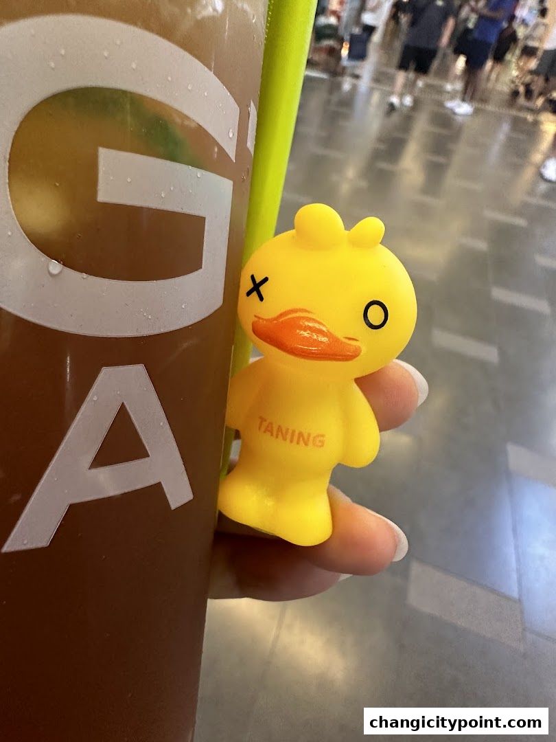 A close-up of a drink with a yellow duck toy with 'TANING' written on it.