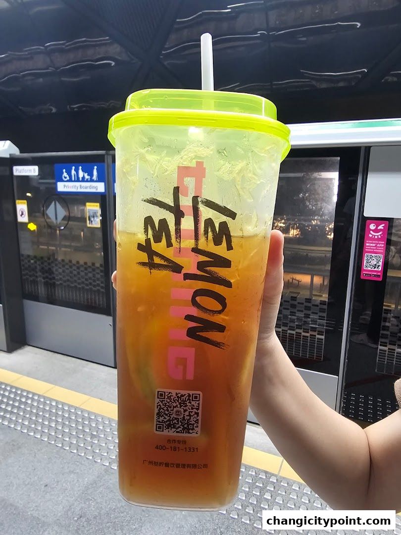 A person holds a large cup of lemon tea with ice and fruit slices.