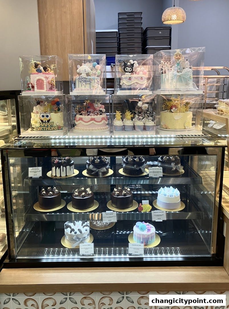 A display case filled with beautifully decorated cakes and cupcakes, featuring cartoon characters and elegant designs.