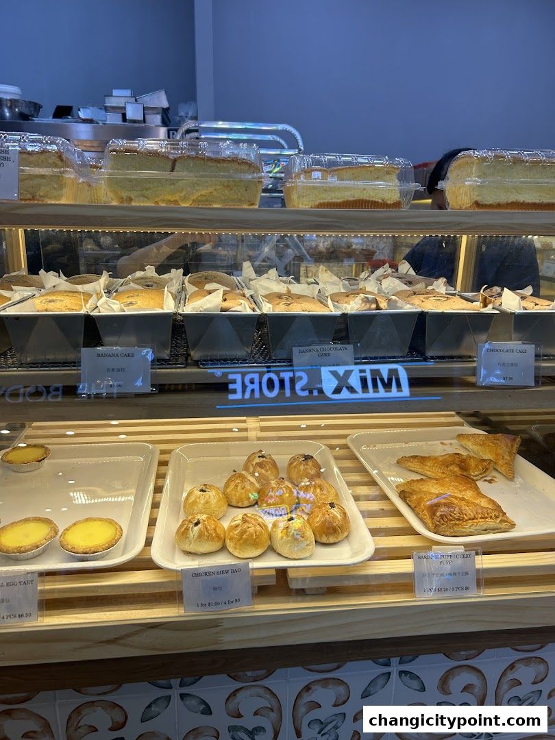 A display case filled with various baked goods including cakes, tarts, and buns.