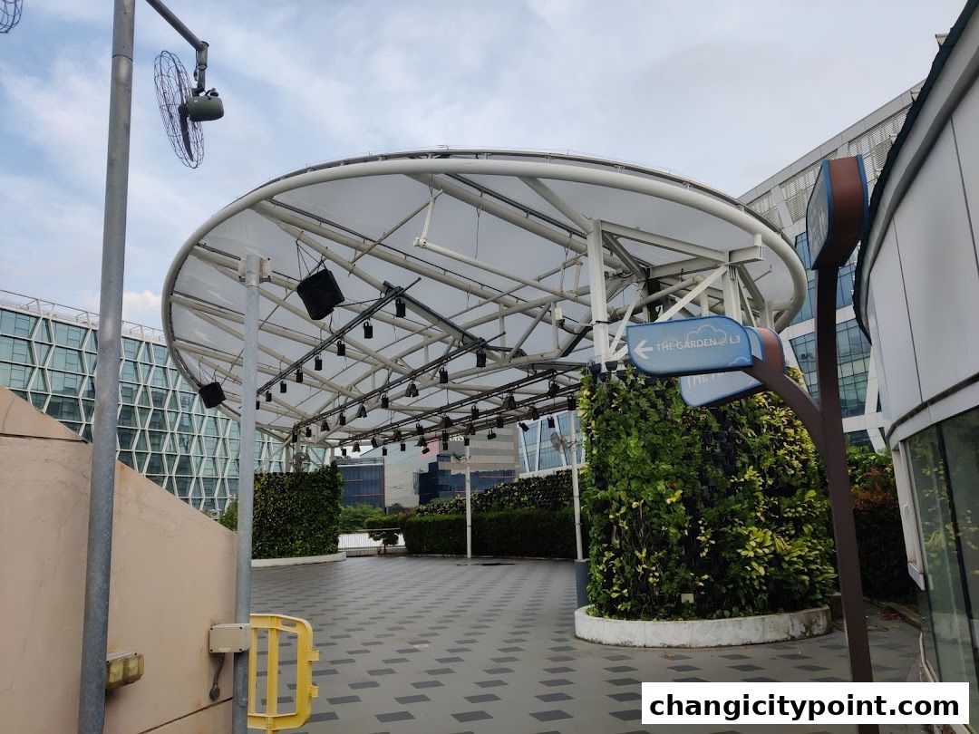 An outdoor covered area with a stage, greenery, and directional signs.