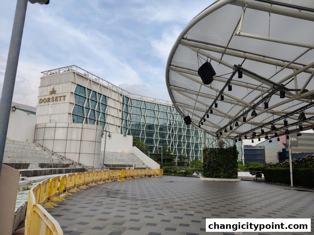 An outdoor plaza with a covered stage area and the Dorsett building in the background.