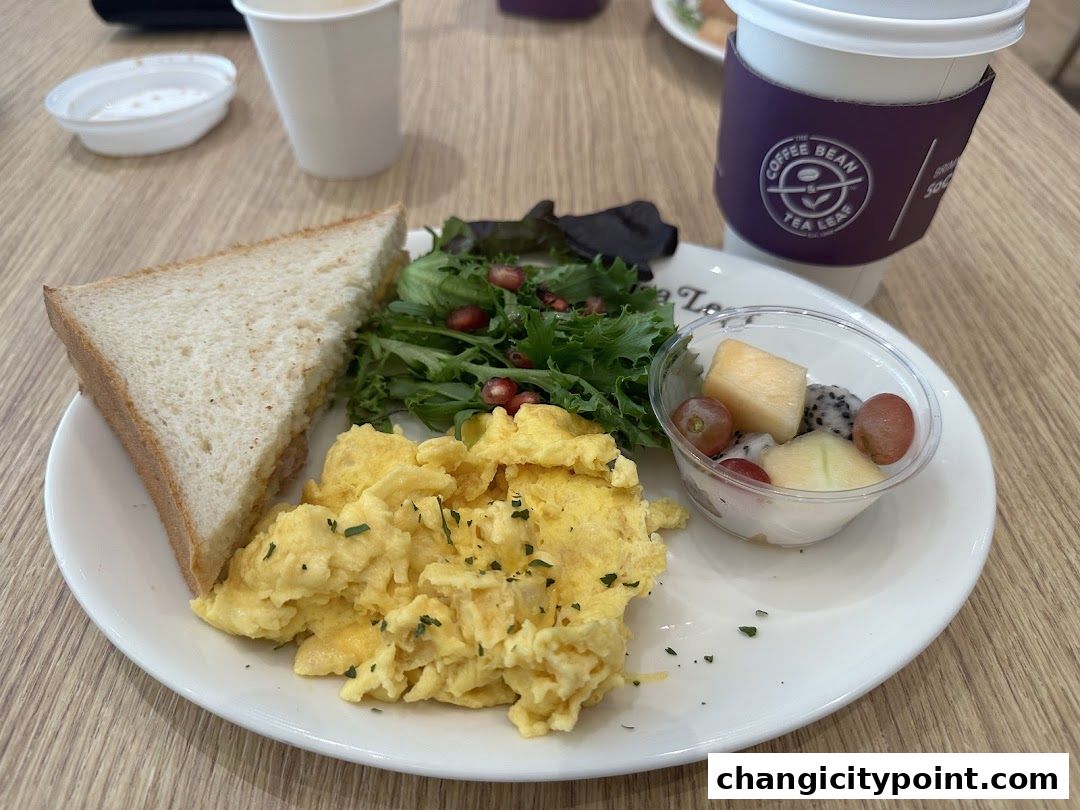 A breakfast plate with scrambled eggs, a sandwich, salad, fruit cup, and coffee.