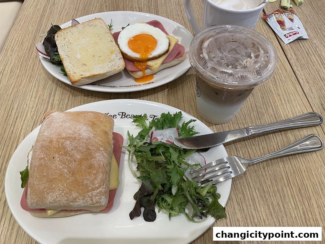 Two plates of food, a sandwich and an open-faced sandwich with egg, and iced coffee.