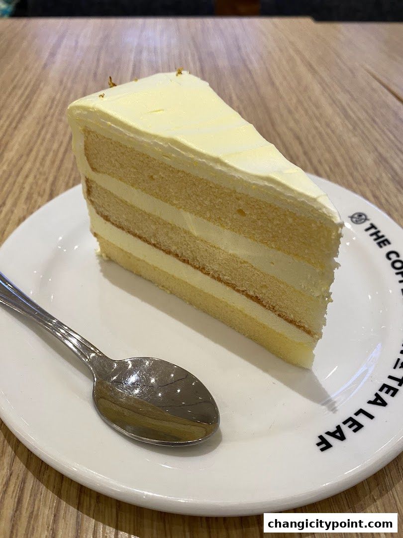 A slice of layered cake with white frosting and a spoon on a plate.