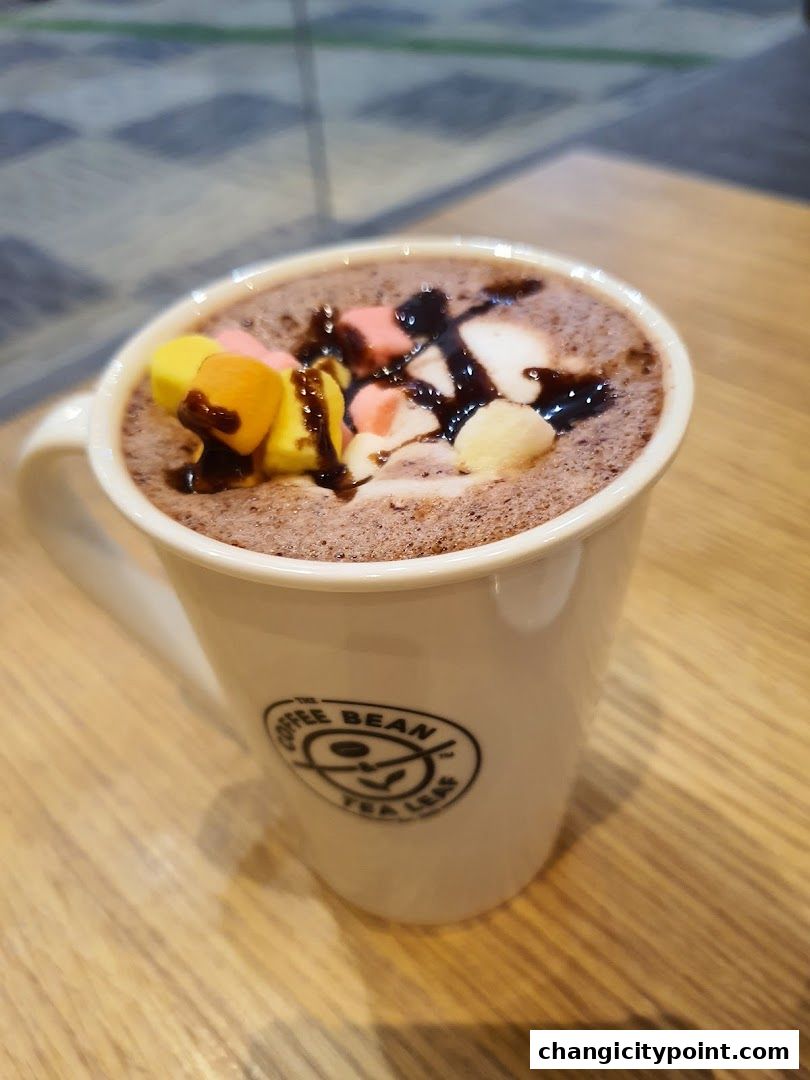 A white mug of hot chocolate topped with marshmallows and chocolate syrup.