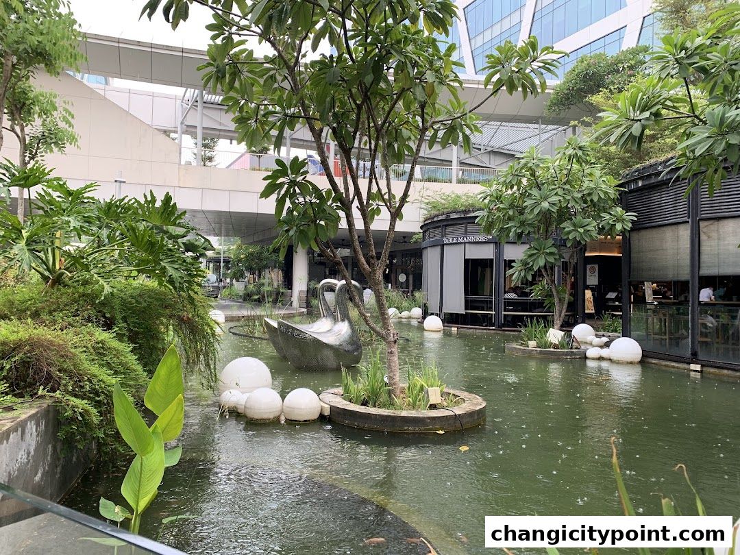 A serene outdoor seating area with a pond, sculptures, and lush greenery.