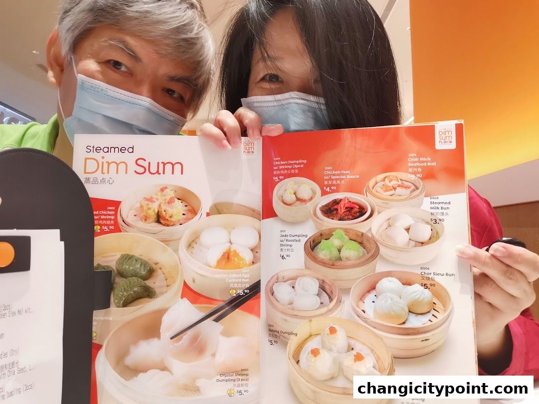 Two people wearing masks hold up a menu featuring various steamed dim sum dishes.