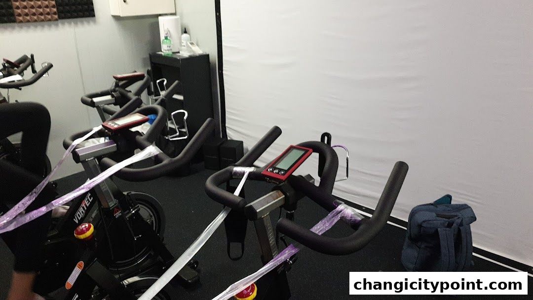 Indoor shot of stationary bikes with purple tape on handlebars and a backpack.