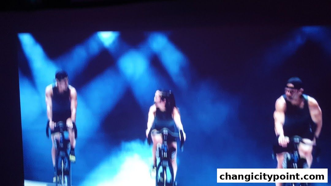 Three people cycling indoors with dramatic blue lighting and smoke effects.