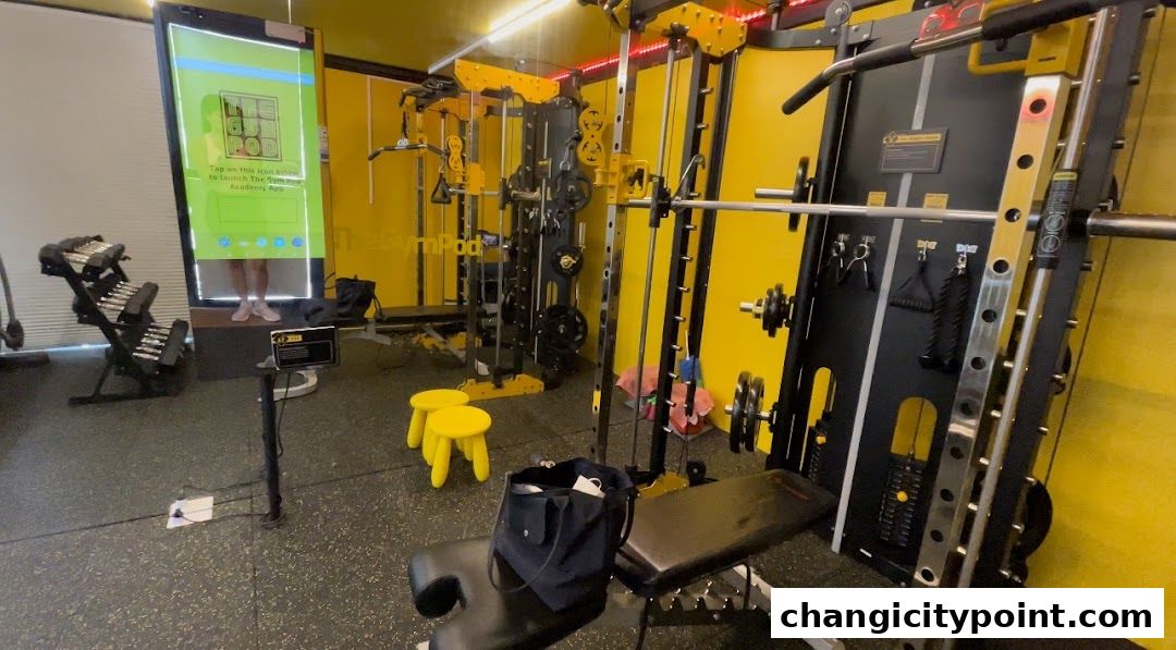 Interior of a modern gym with yellow walls and various weightlifting equipment.