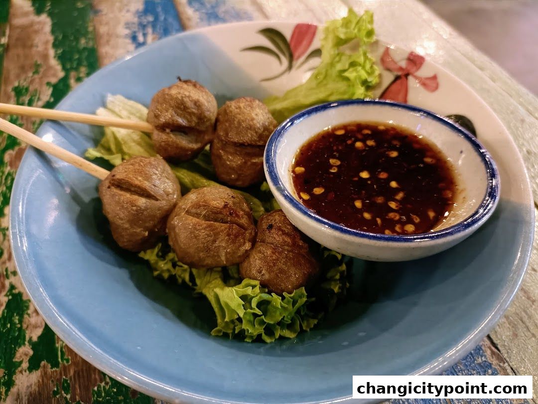 A plate of grilled meat skewers with a dipping sauce and lettuce.