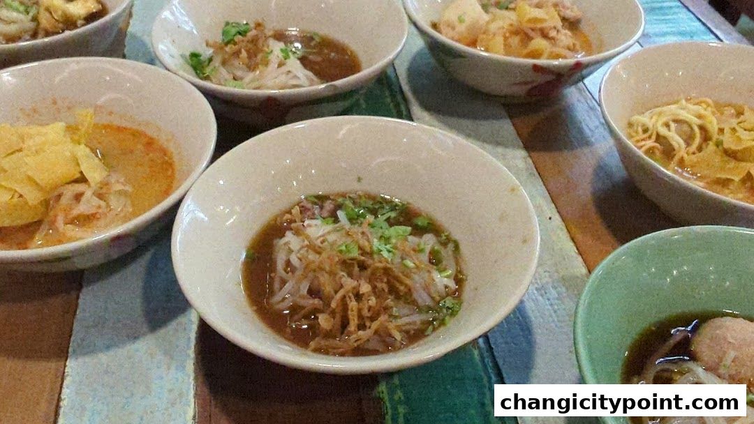 Several bowls of boat noodles with various toppings and broths are arranged on a colorful wooden table.
