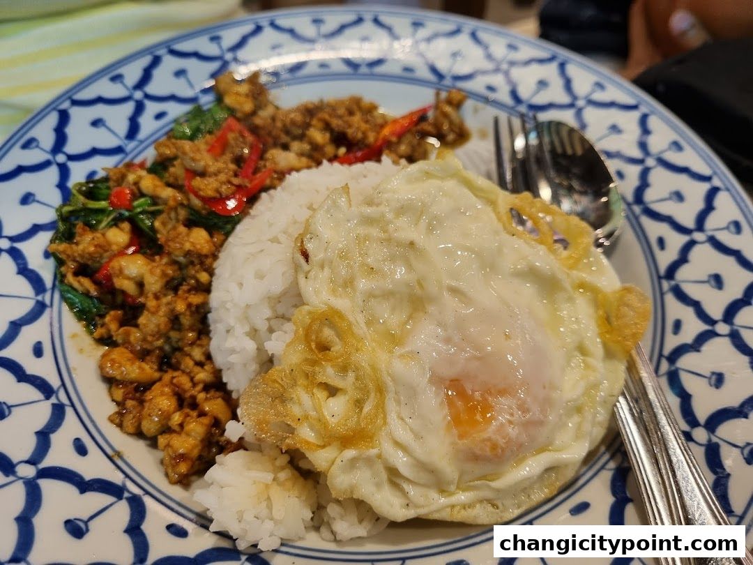 A plate of rice topped with stir-fried meat, basil, chili, and a fried egg.