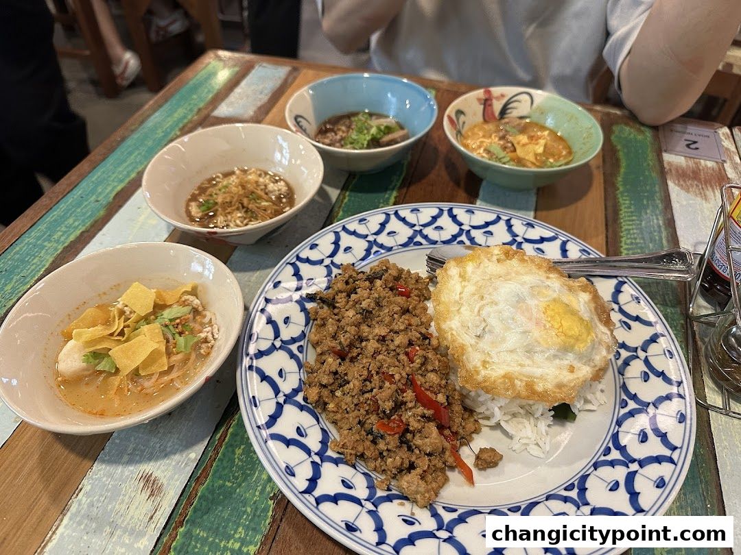 A table laden with various bowls of noodles and a plate of rice with a fried egg.