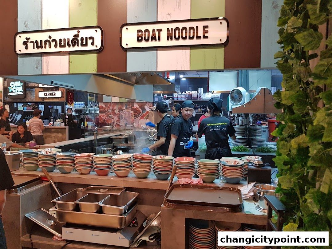 Interior of The Original Boat Noodle shop with staff preparing food and stacks of bowls.
