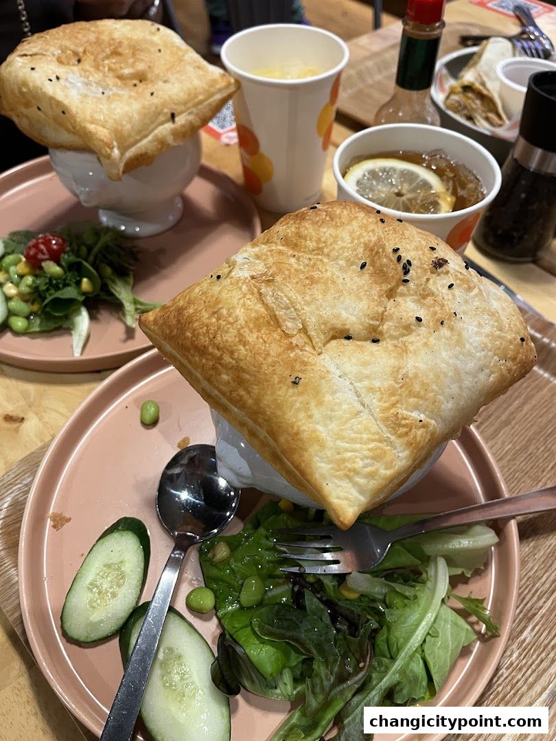 Two servings of soup topped with golden puff pastry, served with salad and drinks.
