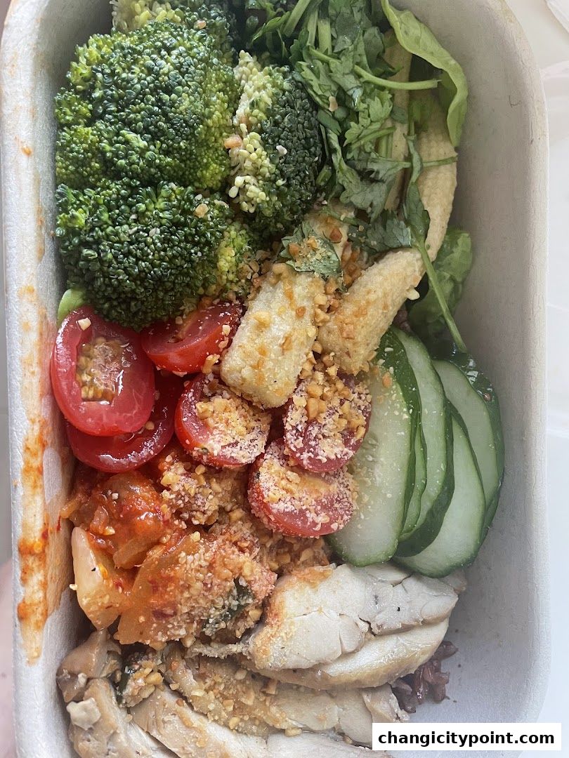 A healthy and colorful bowl of food with chicken, broccoli, tomatoes, cucumber, and corn.