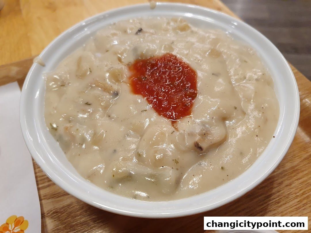 A close-up of a creamy soup with a dollop of red sauce in a white bowl.