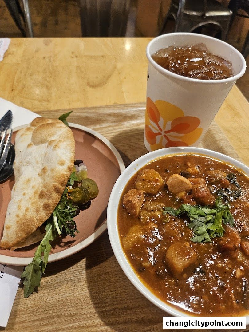 A hearty bowl of stew and a folded flatbread with greens and pickles, served with iced tea.