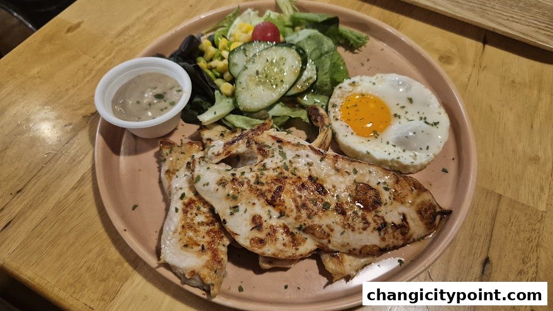 A plate of grilled chicken breast with a fried egg, salad, and dipping sauce.