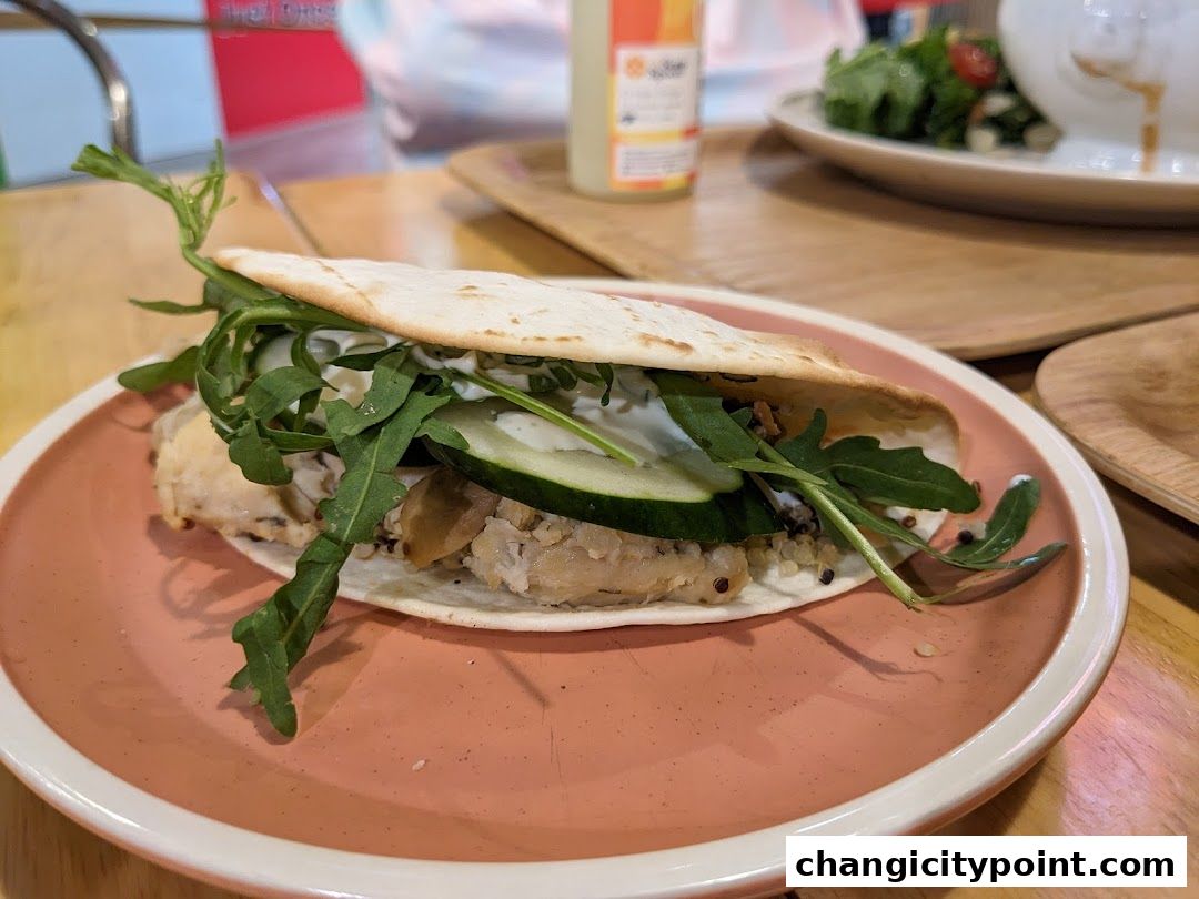 A close-up of a delicious wrap filled with chicken, cucumber, and greens on a pink plate.