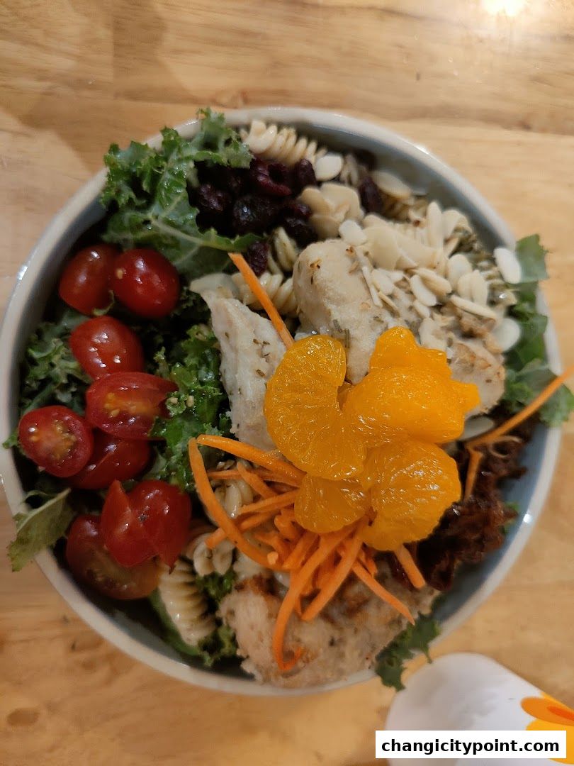 A vibrant salad with chicken, pasta, kale, tomatoes, oranges, and almonds.