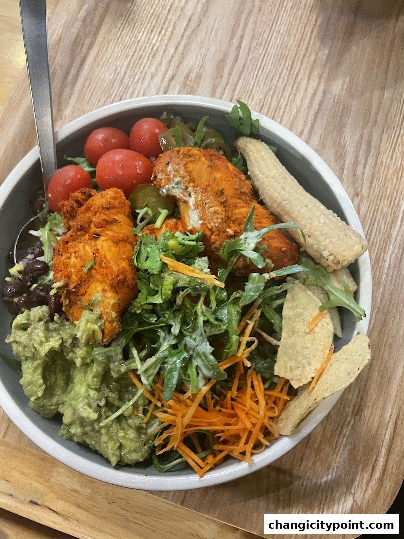 A delicious bowl of food with chicken, guacamole, tomatoes, corn, and salad.