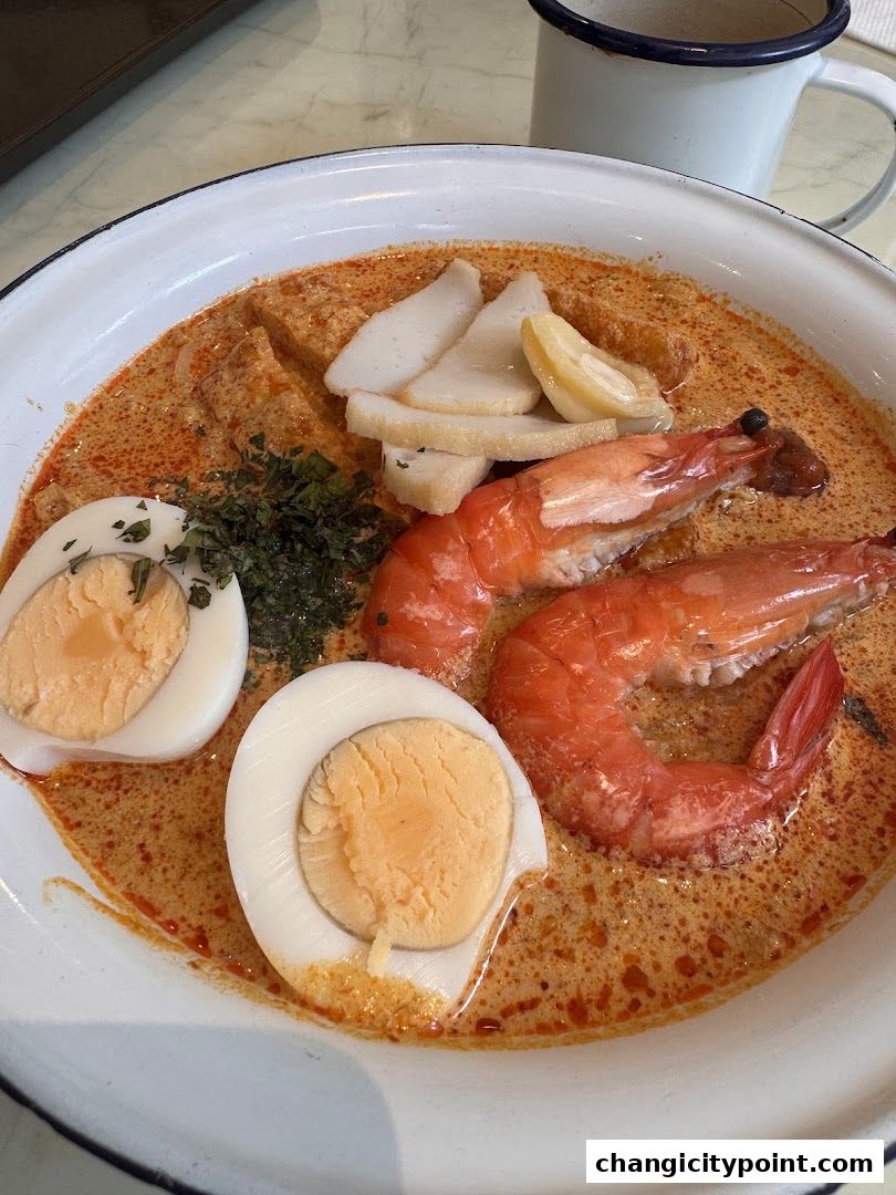 A close-up of a delicious bowl of Laksa with prawns, egg, and fish cake.