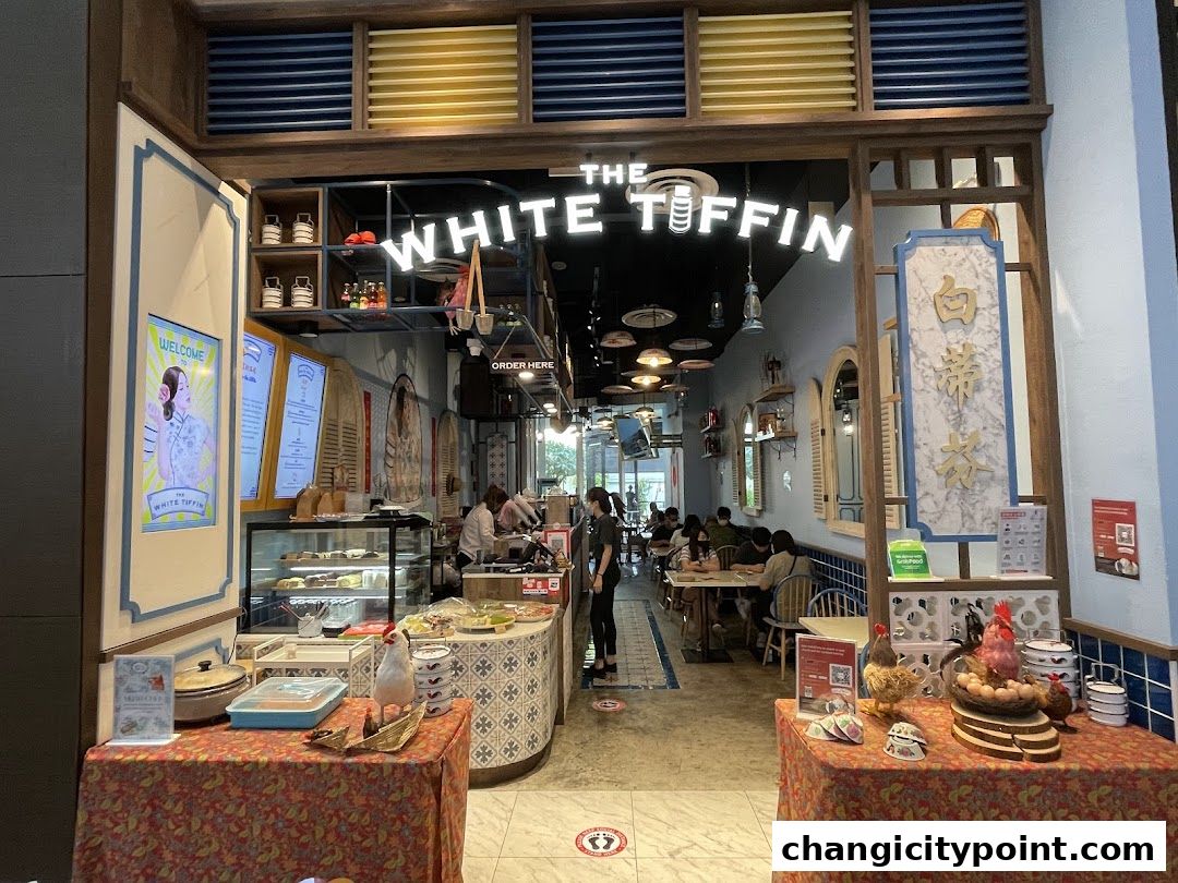 The White Tiffin Changi City Point shop entrance with display tables and seating area inside.