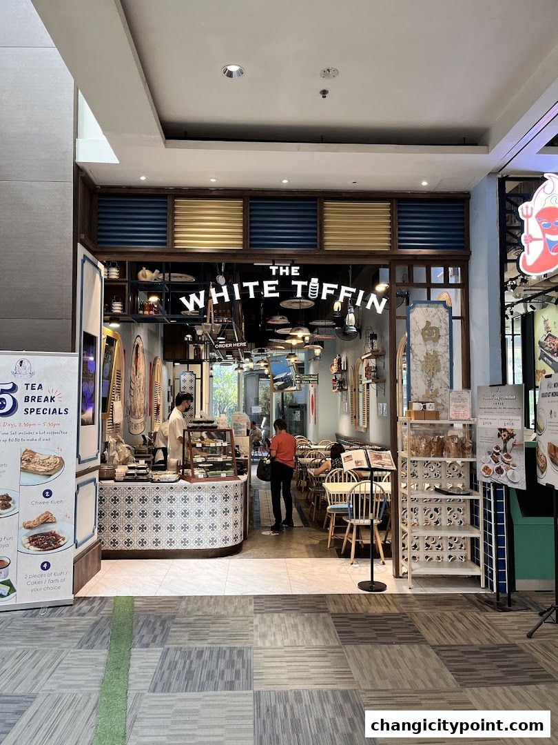 The White Tiffin Changi City Point shop entrance with display cases and seating area.