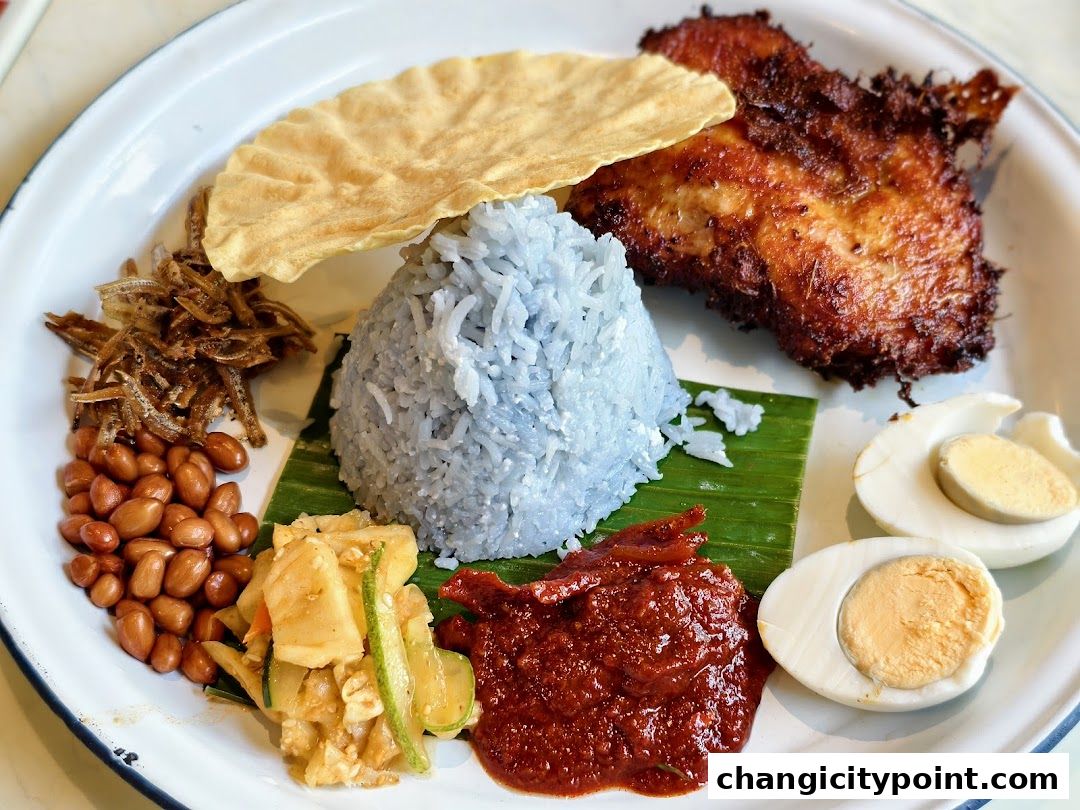 A plate of Nasi Lemak with fried chicken, blue rice, peanuts, anchovies, and egg.