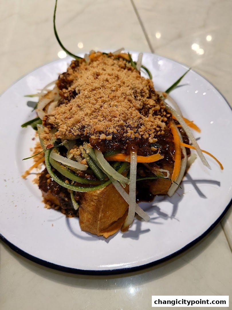 A plate of fried tofu with vegetables and crushed peanuts, drizzled with sauce.