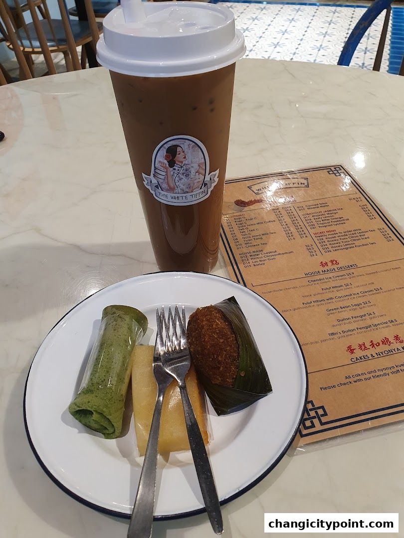 A tall iced coffee drink and a plate of traditional snacks with a menu on the side.