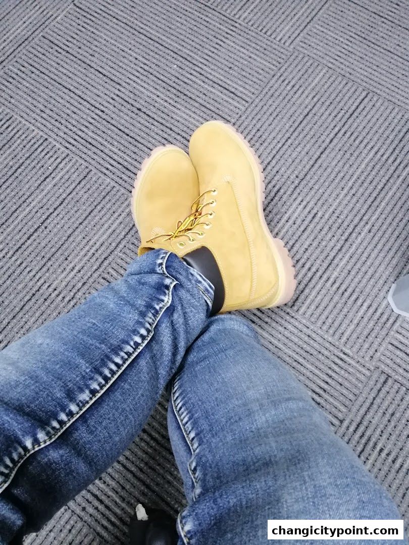 A person wearing yellow Timberland boots and blue jeans sitting on a carpeted floor.