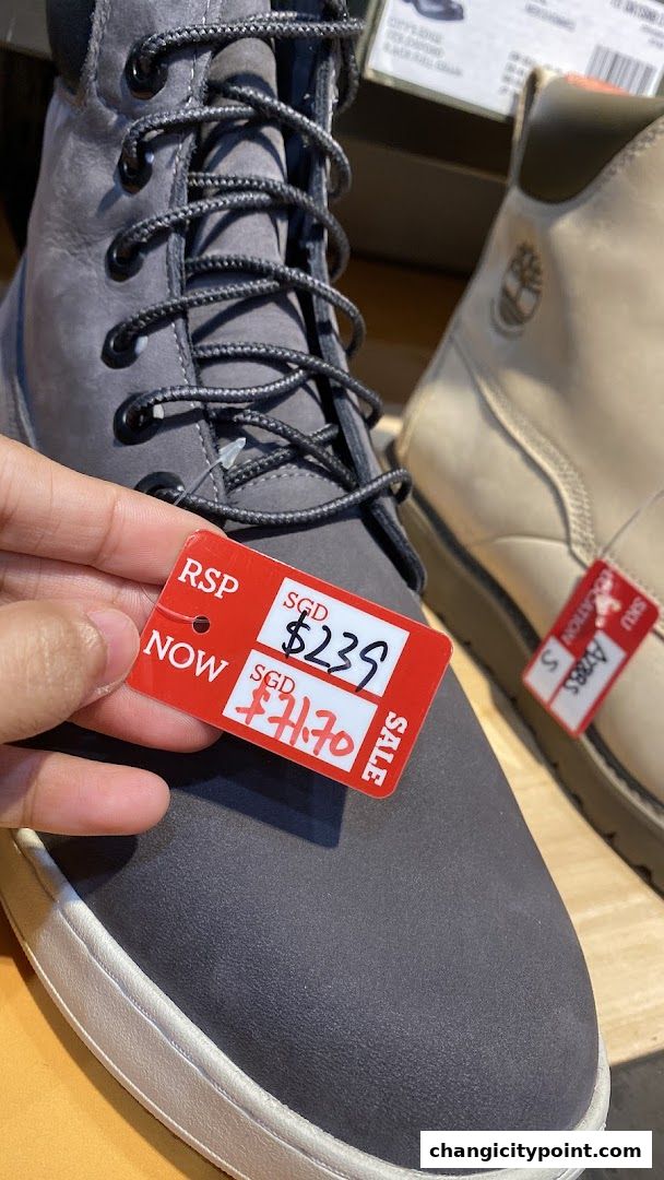 A hand holds a red sale tag on a pair of grey Timberland boots.