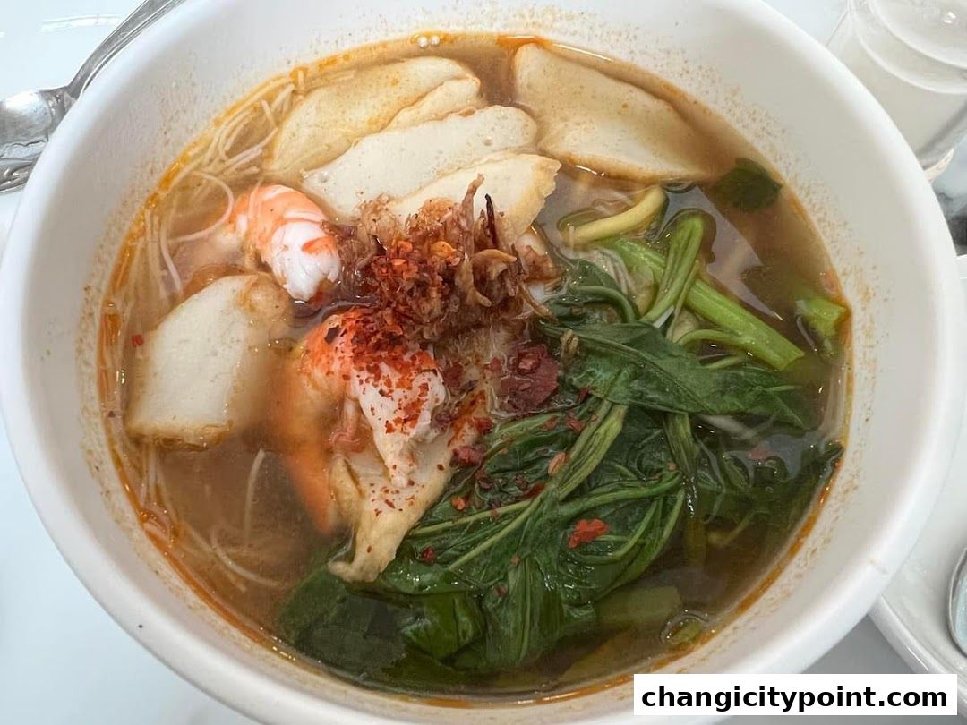 A close-up of a steaming bowl of noodle soup with shrimp, fish cakes, and vegetables.