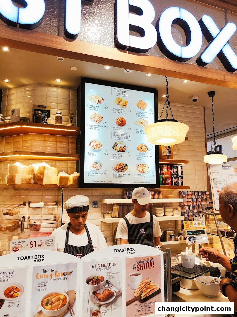 Toast Box interior with staff serving customers and a menu board displaying food items.