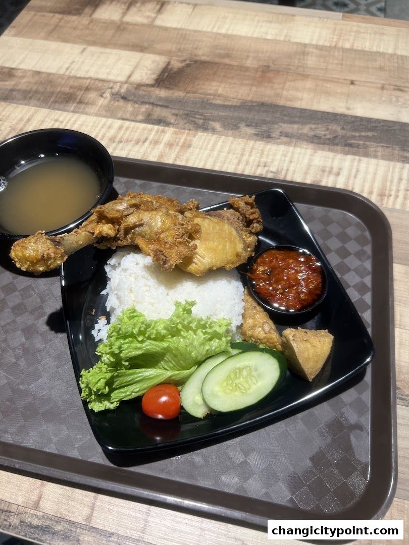 A plate of fried chicken with rice, chili sauce, and fresh vegetables.