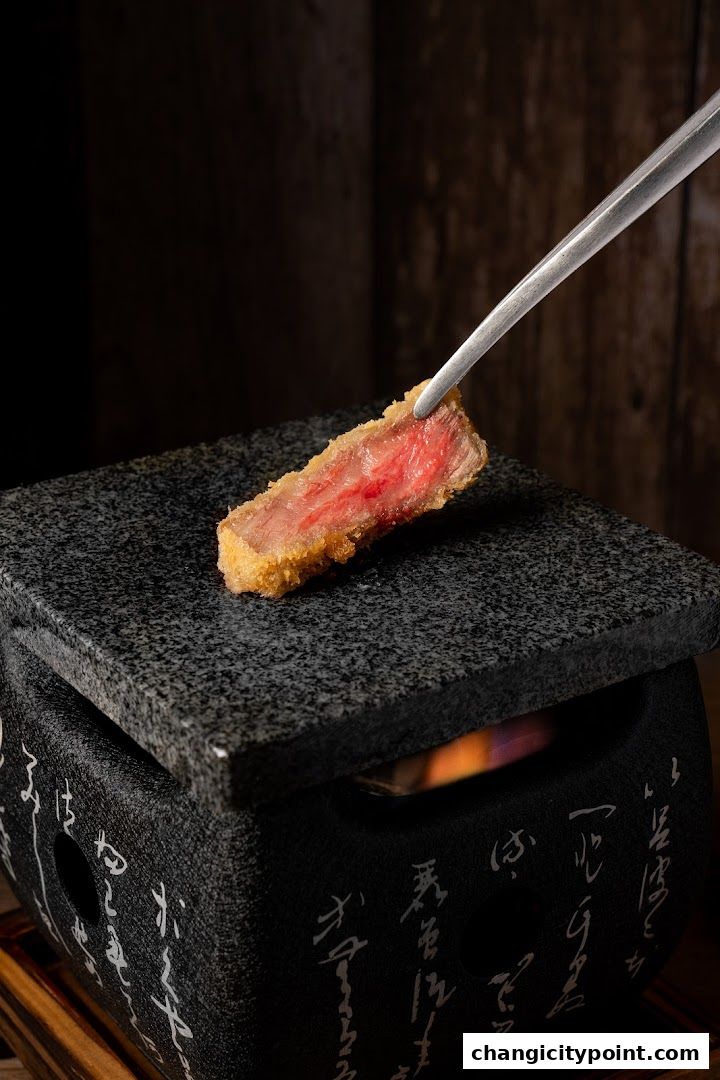 A piece of breaded and fried meat is held by tongs over a hot stone grill.