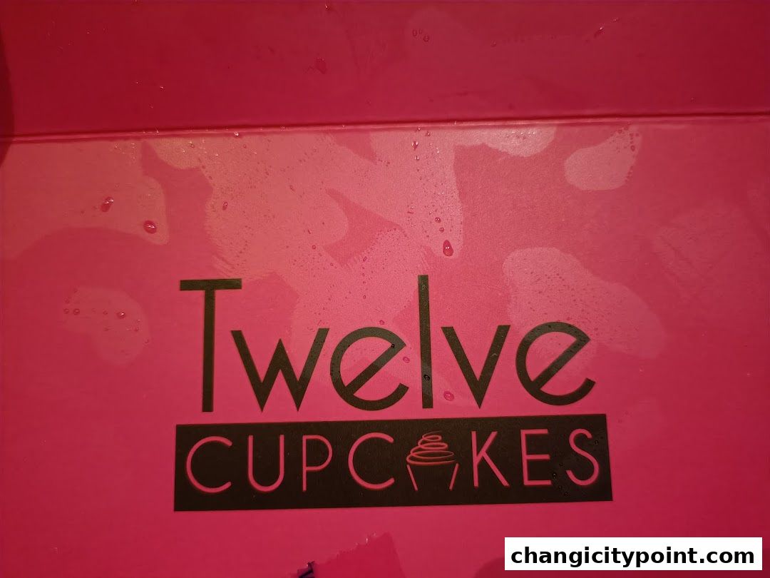 The logo of "Twelve Cupcakes" is displayed on a bright pink surface.
