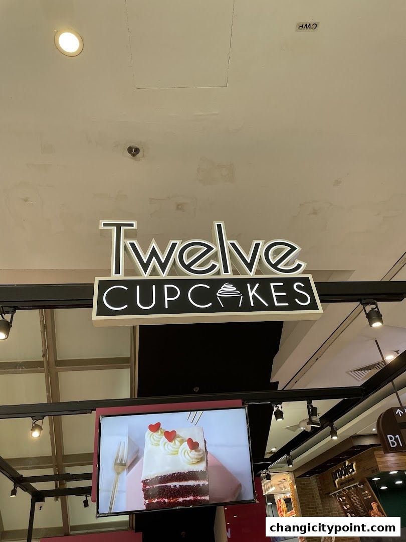 The 'Twelve Cupcakes' sign is illuminated above a screen displaying a slice of red velvet cake.