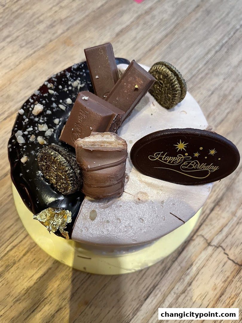 A decadent chocolate and cream cake decorated with Kit Kat bars and a 'Happy Birthday' topper.