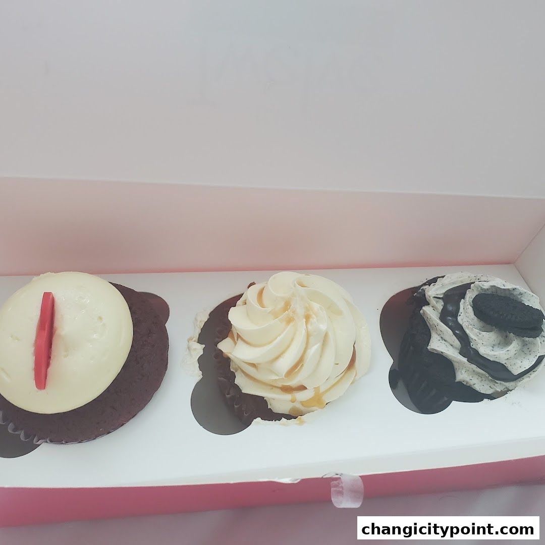 A box containing three delicious cupcakes with various toppings and frosting.