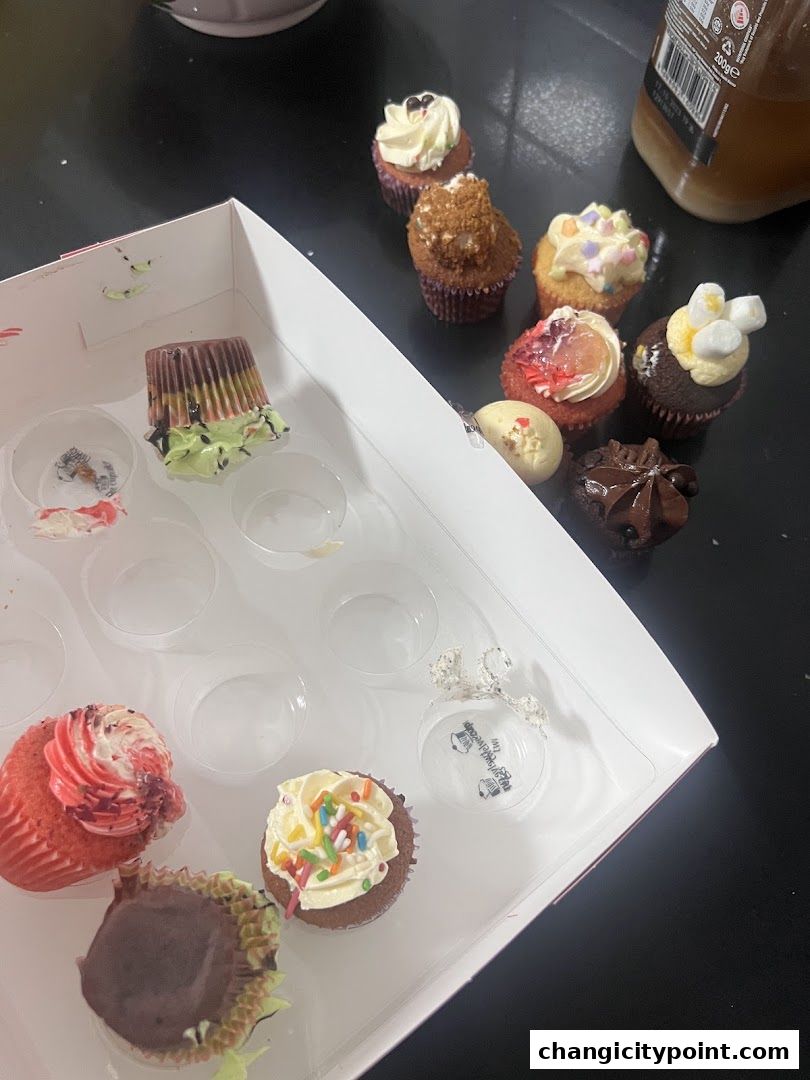 A box of assorted cupcakes, some in the box and some scattered around.